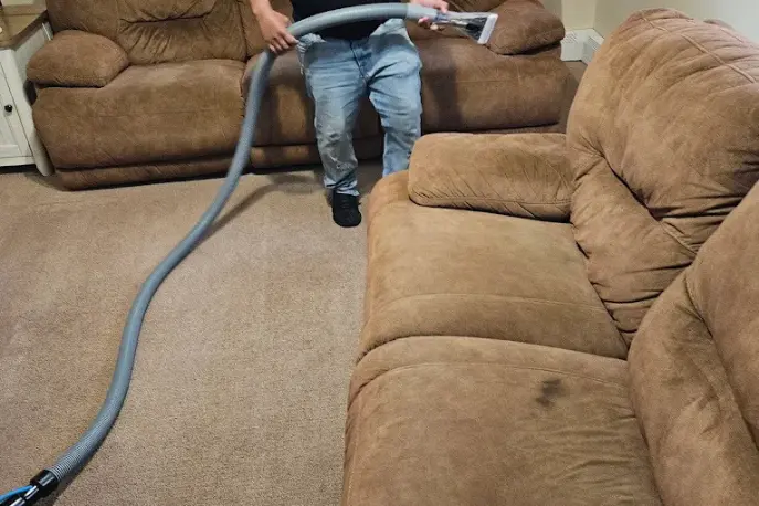 Technician cleaning a fabric sofa with a hot water extraction wand and hose