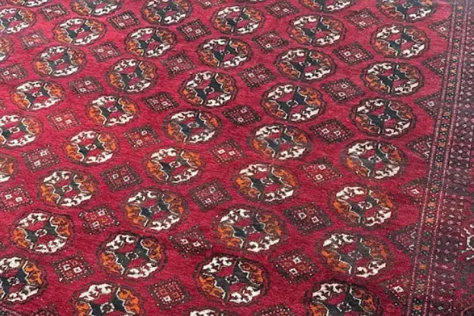Close-up of a red wool area rug with a traditional pattern before professional cleaning